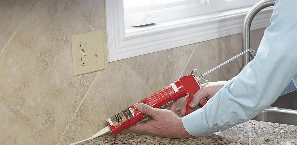 Handyman applying caulk along a kitchen backsplash and countertop seam in Springfield, MO