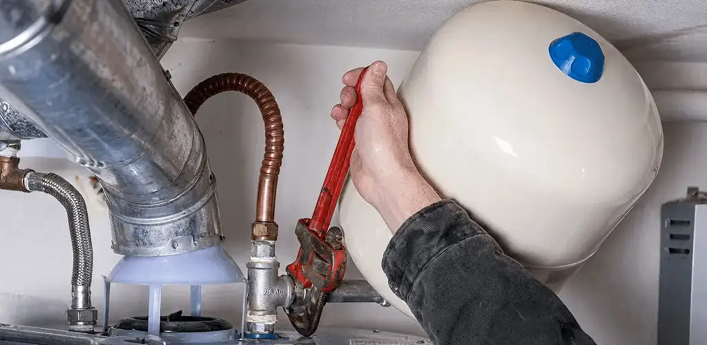 Water heater repair technician tightening plumbing connections near a tank unit in Springfield, MO